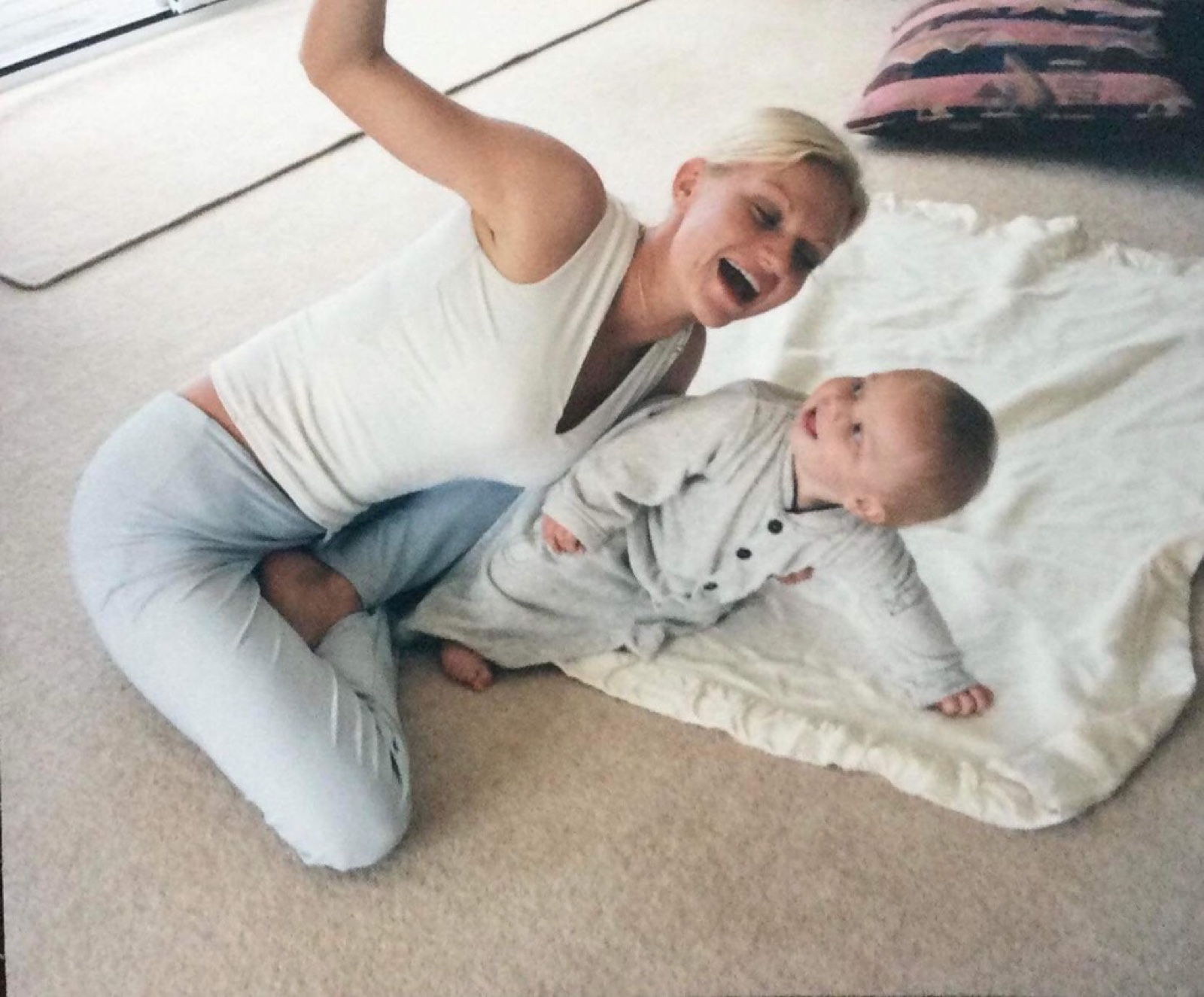 Alysha laughing while playing with her baby son on the floor